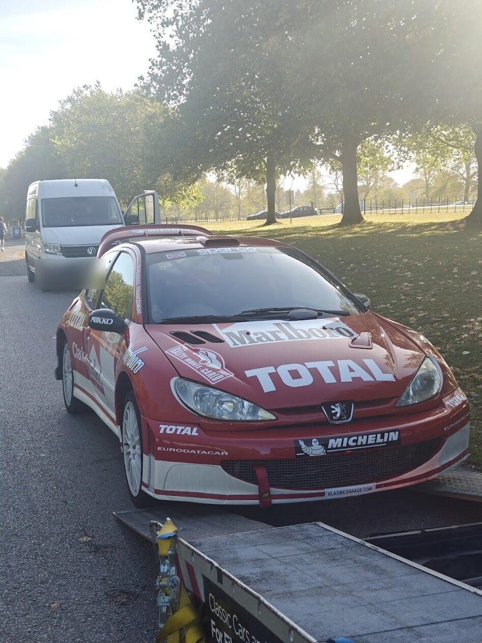 Peugeot 206 WRC being unloaded from a transporter ramp in a tree-lined park