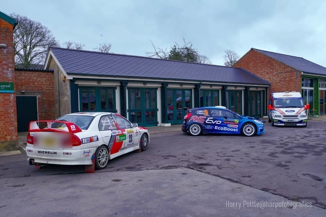 The Evo IV and a Ford rally car with a rally support van outside a motorsport venue
